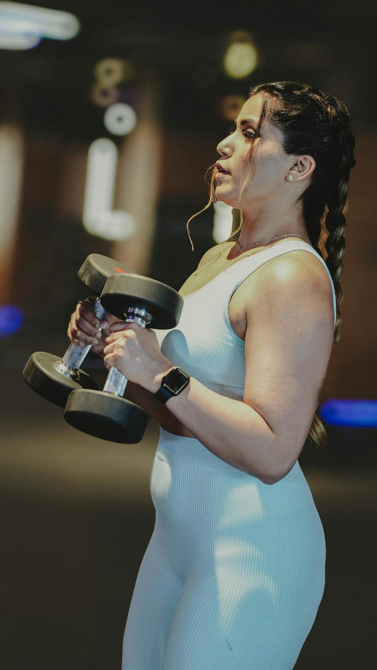  Woman in light blue ribbed activewear lifting weights at the gym, showing comfortable fit and confidence — ideal for workouts on bloated or low-energy days
